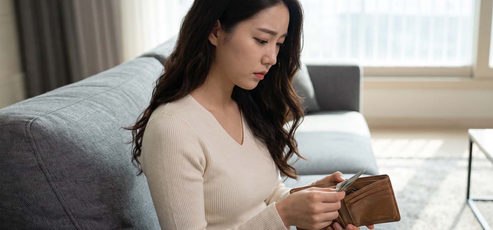 거실 소파에 앉아 빈 지갑을 열어보며 생활비를 고민하는 모습